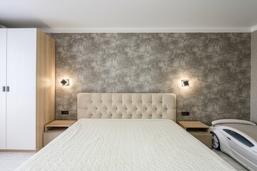 modern bedroom with a beige button-tufted headboard, geometric wall sconces, and palm-leaf...