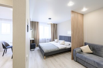 modern, light-filled studio apartment with a gray bed, couch, and wooden slat partition. A separate...