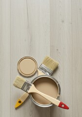 Open paint can with two brushes on wooden floor. Renovation and home improvement concept for interior painting project supplies for banner or poster with copy space. Top view.