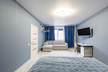 cozy room features blue walls, a sofa by the window, a TV, and a desk. The room is furnished with a...