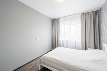 bright bedroom with gray walls, wood flooring, and a white bed. Window with sheer white and gray...