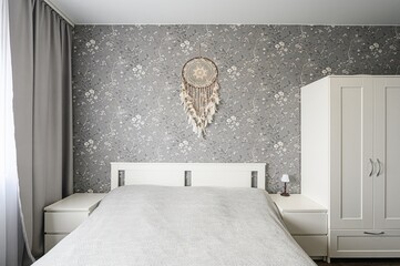 cozy bedroom featuring a white bed, matching nightstands and wardrobe. A dreamcatcher hangs above...