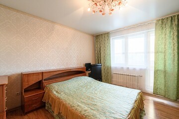 cozy bedroom with a wooden bed, patterned wallpaper, and green curtains. A chandelier hangs from...