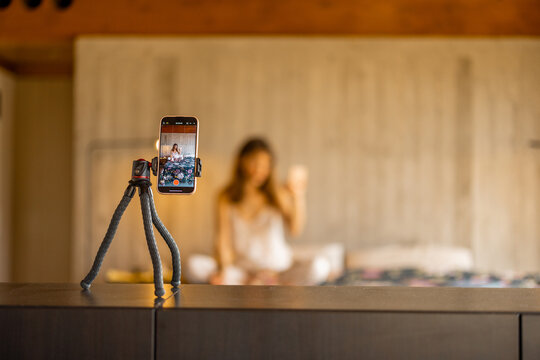 A smartphone on a tripod captures a woman in pajamas creating video content. Great for illustrating influencer work, home blogging, or remote lifestyle content creation