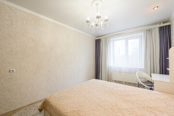 bright bedroom featuring a bed with a patterned beige bedspread, a window with curtains, and a chandelier
