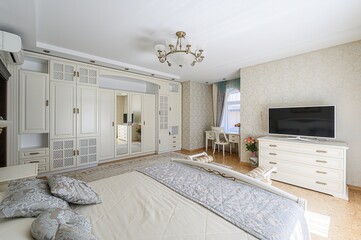 well-lit bedroom features a large wardrobe, a TV on a chest of drawers, and a cozy bed with...
