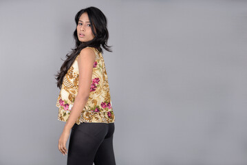 A charming young woman wearing a floral patterned top, black leggings and black heels, posing with...