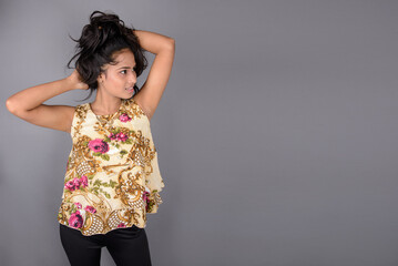 A charming young woman wearing a floral patterned top, black leggings and black heels, posing with...