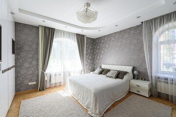 modern bedroom featuring a large bed, textured wallpaper, elegant curtains, and a crystal...