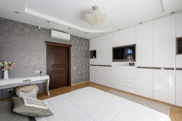 Bright bedroom with white wardrobe & desk, floral wallpaper, wooden door, and a modern bed. Chandeliers hanging from the ceiling