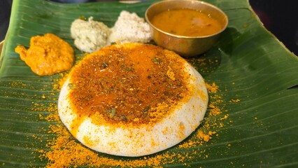 Tasty Ghee pudi Thatte idli served in restaurant hotel on table. Ghee podi thatte idli with three types of chutney and sambar on banana leaf from dvg benne dosa restaurant from Bengaluru