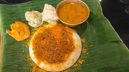 Top view of Tasty Ghee pudi Thatte idli served in restaurant hotel on table. Ghee podi thatte idli with three types of chutney and sambar on banana leaf from dvg benne dosa restaurant from Bengaluru