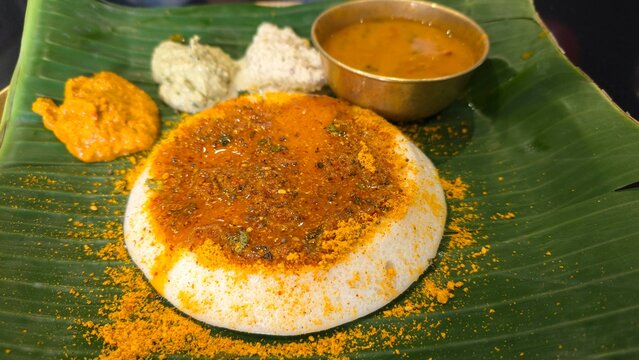 Tasty Ghee pudi Thatte idli served in restaurant hotel on table. Ghee podi thatte idli with three types of chutney and sambar on banana leaf from dvg benne dosa restaurant from Bengaluru