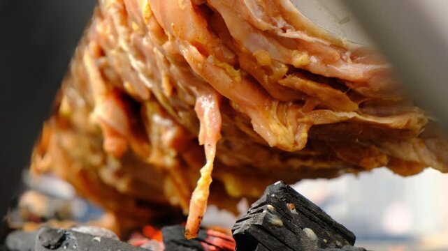 Slow rotation of a horizontal spit with multiple pieces of meat over burning coals releasing smoke. Cooking hot grilled meat for street fast food like shawarma in lavash or sandwich buns.