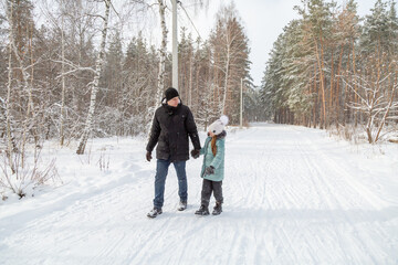 Dad and daughter walking and having fun in snowy winter forest
