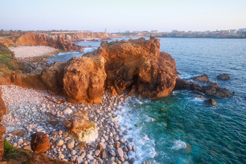 Sunny rocky coastline of Atlantic Ocean in the rays of setting sun, Papoa Island, Peniche, Portugal