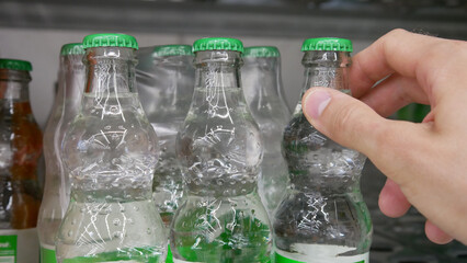 Close-up of a customer's hand taking a glass bottle of soda