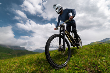 Fototapeta premium Mountain biker riding down a grassy slope. Enduro mountain bike. MTB against a mountain landscape