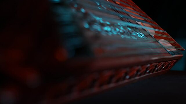 Cinematic macro close-up of a traditional wooden stringed instrument. Slow focus pull along tuning pegs and strings under dramatic red and teal lights, creating a moody atmosphere.
