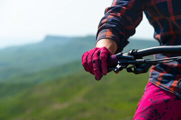 Close-up of mountain mtb bike handlebars against a mountain landscape in defocus. Rider's hand on the handlebars. Mountain downhill cycling. Copy space background for cycling