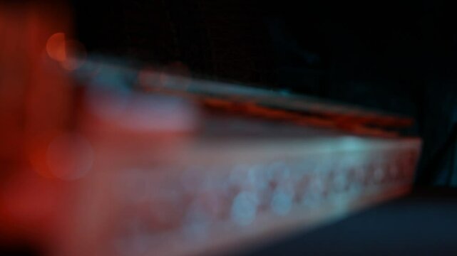 Cinematic macro close-up of a traditional wooden stringed instrument. Slow focus pull along tuning pegs and strings under dramatic red and teal lights, creating a moody atmosphere.