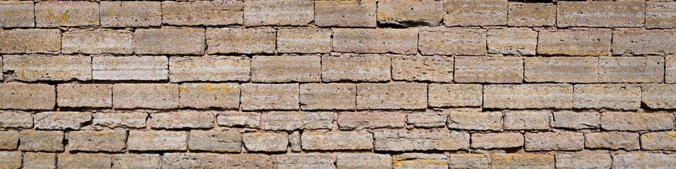 A wide format photo of a wall of a yellow limestone brick facade on a bright sunny day