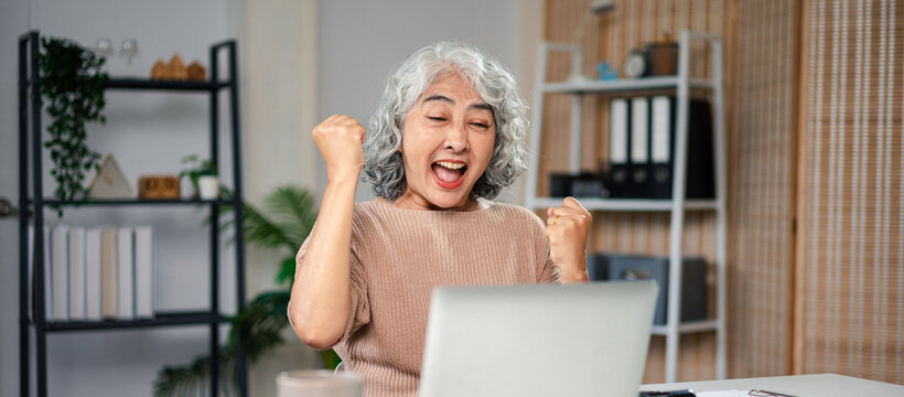 Excited Older Asian Woman Celebrating Success on Laptop Computer at Home Office | Achievement Goal and Happy