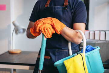 Housekeeping and cleaning concept, Happy young man in orange rubber gloves wiping dust using mop while cleaning on floor at home