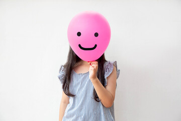 little girl holding pink smile face balloon; Happiness and positive emotion
