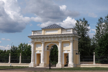 Obraz premium Captivating image of an elegant historic archway, framed by a vintage lamp post under a partly cloudy sky. Stunning architectural details and lush landscape provide a timeless charm.