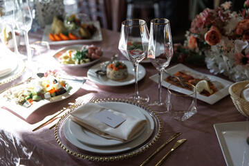 Luxurious table setting with crystal glasses, elegant cutlery, and beautifully arranged plates. The arrangement features floral centerpieces and gourmet appetizers, perfect for upscale events.