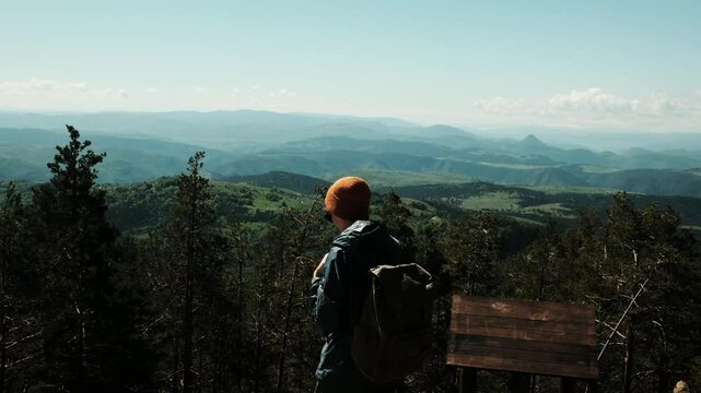 Young woman hiker with backpack and orange hat stretches her arms wide while enjoying a panoramic mountain view from Tornik peak in Zlatibor, Serbia during spring. Solo travel concept