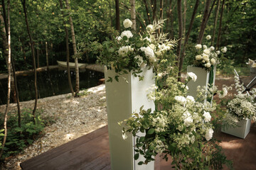  Lush white flowers and greenery in an elegant arrangement set against a tranquil forest backdrop. The combination of natural elements creates a serene and harmonious atmosphere.