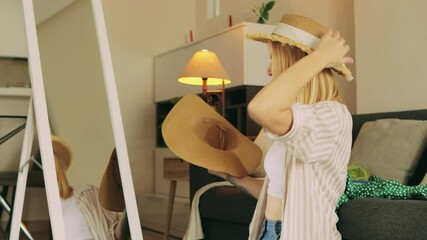 Woman selecting stylish straw hats near mirror, reflecting summer vacation preparation, finding ideal headwear for sunny travel moments.Traveling and vacation concept