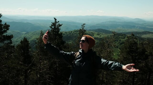 Female traveler taking selfie with breathtaking spring landscape in the background, standing confidently above the forest in Zlatibor, Serbia country. Travel blogger making video outdoor