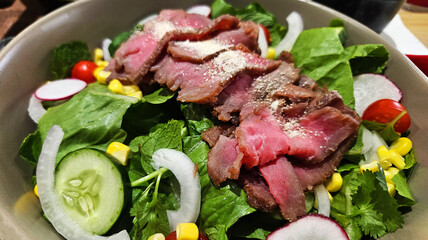 Close up sliced beef or meat salad on fresh vegetables, cucumber, lettuce, tomato, corn, onion and cabbage in white bowl. Healthy food for life and low calorie meal.