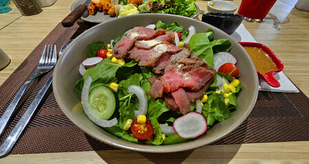 Sliced beef or meat salad on fresh vegetables, cucumber, lettuce, tomato, corn, onion and cabbage in white bowl. Healthy food for life and low calorie meal.