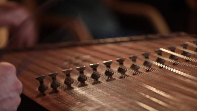close-up shows a woman's hands playing an ornate wooden zither with plectrums. A microphone captures the beautiful sound of this traditional Middle Eastern folk instrument.