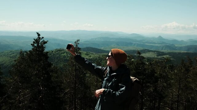 Female traveler taking selfie with breathtaking spring landscape in the background, standing confidently above the forest in Zlatibor, Serbia country. Travel blogger making video outdoor