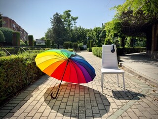  White chair with headphones and rainbow umbrella in a sunny park