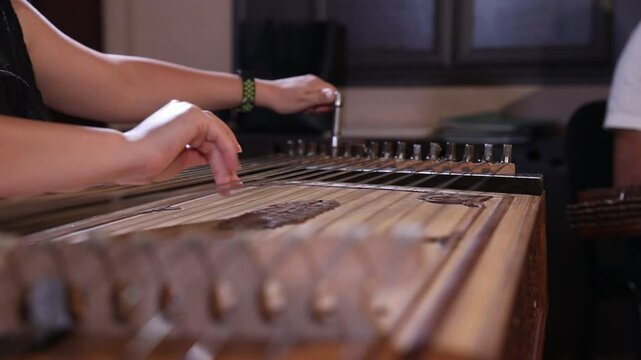 close-up shows a woman's hands playing an ornate wooden zither with plectrums. A microphone captures the beautiful sound of this traditional Middle Eastern folk instrument.