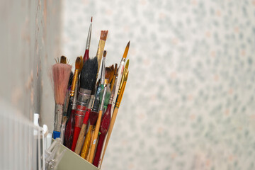 Assorted paintbrushes for artwork stored in a wall-mounted holder, showcasing an artist's creative tools