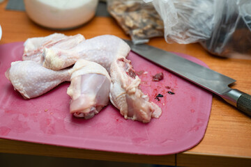 Chopped chicken drumsticks on a plastic cutting board with a knife nearby, ready for cooking preparation