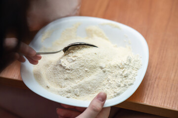 Mixing semolina flour with sugar using a metal spoon in a white ceramic bowl for cake preparation on a kitchen table