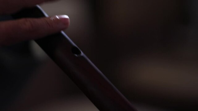 Close-up on a musician's hands preparing to play a traditional woodwind instrument, possibly a duduk. He places it on a music stand and adjusts his fingering.