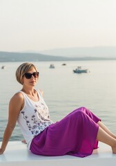 Elegant Woman in Purple Skirt Relaxing by Serene Coastal Waters at Golden Hour