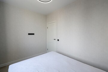 minimalist bedroom interior with textured light walls, a white bed, a white door, and a modern...
