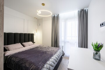 modern bedroom featuring a bed with a gray headboard, gray curtains, white walls, and a contemporary ring-shaped light fixture