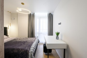 modern bedroom features a bed with a plush purple blanket, a white desk, and stylish lighting