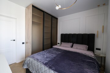 modern bedroom with a large bed, dark headboard, sliding door wardrobe, pendant lights, and neutral decor